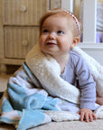 Baby wrapped in a soft blanket sitting on a carpeted floor.