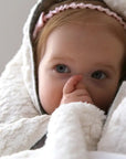 Child wrapped in a white blanket with a pink headband, looking directly at the camera.